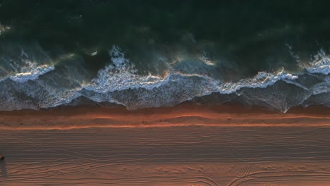 A-stationary-birdseye-view-shot-of-the-shoreline-with-strong-waves-of-water-during-the-golden-hour