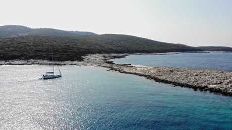 Motoryacht,-Die-Im-Sommer-In-Griechenland-In-Der-Nähe-Der-Felsigen-Küstenlinie-Des-Strandes-Mit-Glitzerndem-Wasser-Schwimmt