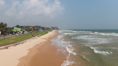 Drohnen-Flyover-Sandiges-Ufer-Und-Flut-Ozeanwellen-Gegenüber-Strandgeschäften-Am-Beliebten-Touristenziel-Mirissa-Beach,-Sri-Lanka