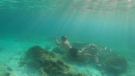 Hombre-Nadando-Bajo-El-Mar-Azul-Con-Rayos-De-Sol