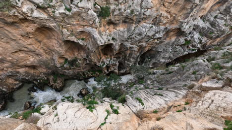 4k-Top-down-shot-of-a-cold-mountain-river-between-tall-cliffs-at-El-Caminito-del-Rey-in-Gorge-Chorro,-Malaga-province,-Spain