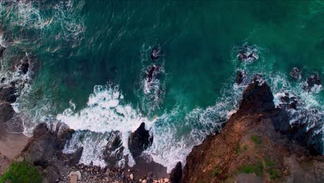 Top-down-aerial-view-from-above-of-ocean-waves-crashing-and-foaming-on-empty-tropical-beach-with-stones