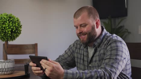 A-Friendly-Looking-Bearded-Young-Adult-Waving-Hand-While-Video-Chatting-With-Someone-On-His-Tablet-At-Home