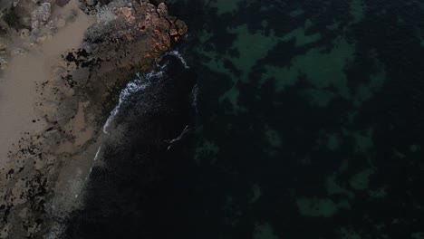 Eine-Aufnahme-Aus-Der-Vogelperspektive-Des-Offenen-Wassers-Mit-Verschiedenen-Wellen,-Die-Auf-Die-Küste-Treffen