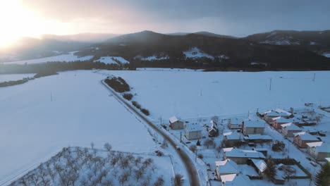 Static-aerial-drone-view-of-small-village-covered-with-snow,-sunrise-behind