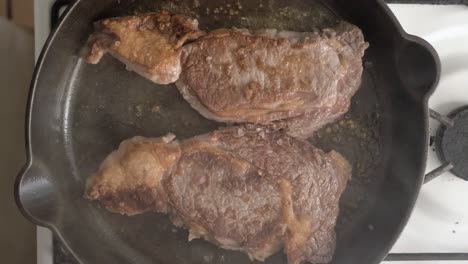 Steaks-fried-and-flipped-in-a-cast-iron-skillet-with-oil---Overhead-view