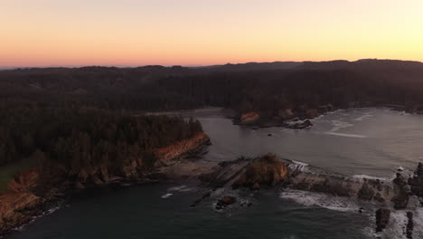 Qochyax-Island,-Sunset-Bay-and-Cape-Arago-Lighthouse-at-the-Oregon-Coast,-aerial-after-sunset-at-dusk