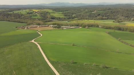 Vuelo-Sobre-Una-Masía-En-La-Costa-Brava-En-Girona-Verde-Campo-Cultivado-Y-Montañas-Amarillas-En-El-Fondo