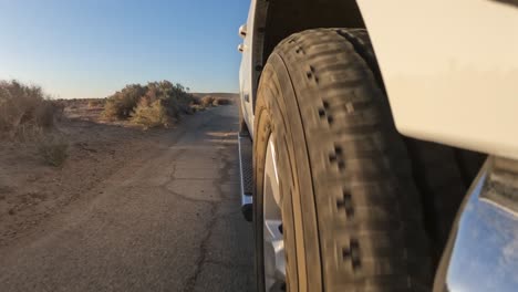 Low-angle-view-from-in-front-of-the-tire-while-driving-down-a-bumpy-road-in-the-Mojave-Desert-at-sunset