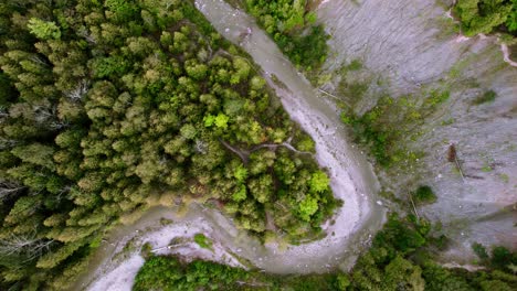 Aerial-overhead-of-Winding-River-cutting-through-dense-forest-landscape-with-eroded-cliff,-rising-shot
