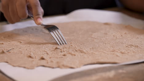 Using-a-fork-to-prick-the-flattened-matzah-dough-so-it-doesn't-rise-when-baked-into-Passover-bread