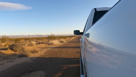 From-the-side-of-a-truck,-looking-down-a-down-a-dirt-road-in-the-rugged-Mojave-Desert