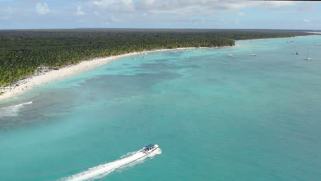 A-powerboat-cruises-across-tropical-azure-waters,-the-Dominican-Republic,-Aerial-panorama-reveal
