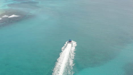 A-luxury-powerboat-motoring-across-the-calm-azure-ocean,-revealing-white-sand-beaches,-aerial