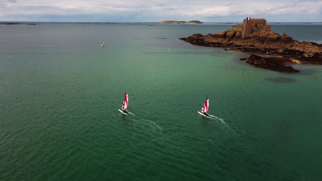 Aerial-view-of-catamaran-boat-race-with-fortress-on-Petit-Be-tidal-island-in-background,-France