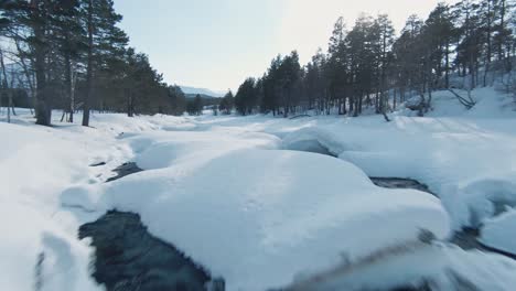 Mountain-river-and-landscape-covered-in-massive-layer-of-snow-in-Norway,-aerial-FPV-fly-backward-view