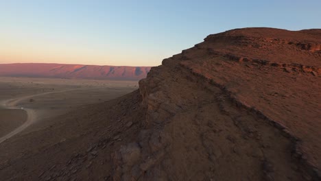 Drohne-Fliegt-über-Felsformation-In-Der-Wüste-Mit-Rotem-Berg-Im-Hintergrund-Bei-Sonnenuntergang,-Marokko
