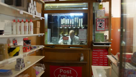 A-post-master-in-a-post-office-labelling-parcels-behind-the-shop-counter