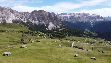 Seceda-and-Val-Gardena-Valley-at-South-Tyrol,-Italian-Alps,-Dolomites,-Italy---Aerial-Drone-View-of-Green-Valley,-Cabins-and-High-Mountains