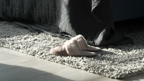 Panning-shot-of-fluffy-slippers-on-bedroom-floor-rug
