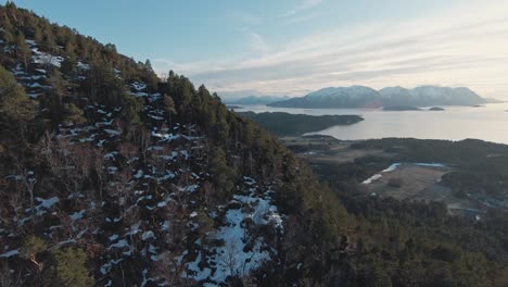 Mountain-landscape-of-Norway-covered-in-pine-tree-forest-and-snow,-aerial-FPV-view