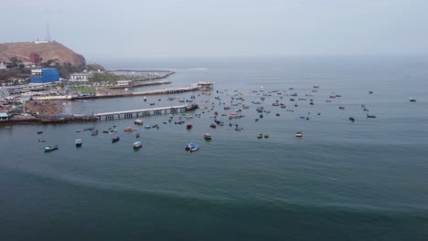Drone-footage,-flying-forwards-from-the-beach-towards-a-harbour-with-many-fishing-boats-and-2-piers