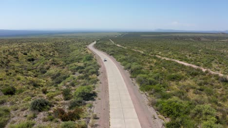 Single-white-car-traveling-narrow-long-road-in-vast-arid-desert