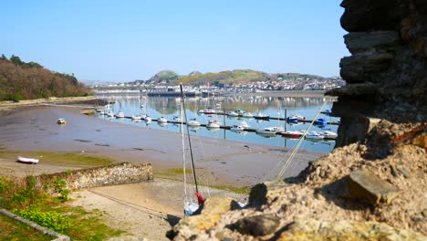 Overlooking-yachts-moored-on-harbour-coastline-view-from-stone-wall-ruins-with-sunny-blue-sky