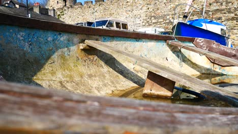 Small-water-filled-aged-fishing-boat-abandoned-on-sunny-shoreline-close-up-inside-vessel