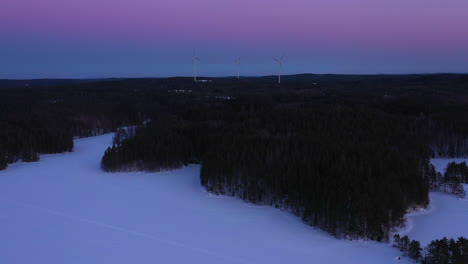 Drone-shot-of-windmills-spinning-in-horizon-on-a-golden-hour-blue-moment-after-sunset-on-a-winter-night