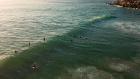 Surfers-Floating-On-The-Ocean-At-Llandudno,-Cape-Town,-South-Africa---aerial-drone-shot