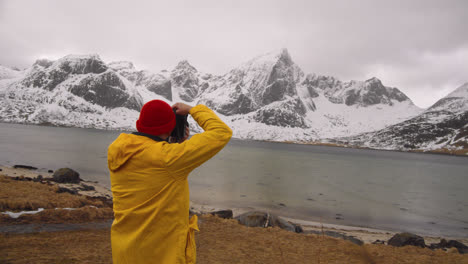 Photographer-In-Yellow-Jacket-Taking-Snapshots-Of-Snowy-Mountains-In-Lofoten-Norway---panning-shot