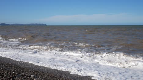 Stormy-windy-ocean-waves-barrel-onto-pebble-beach-Welsh-coastline-shore