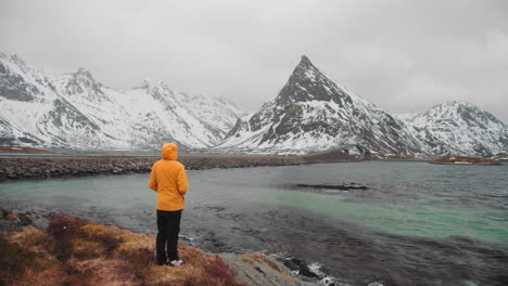 Man-In-Yellow-Jacket-Walking-Towards-Edge-Of-The-Coast-To-Admire-Beautiful-Winter-Scenery-In-Norway---wide-shot