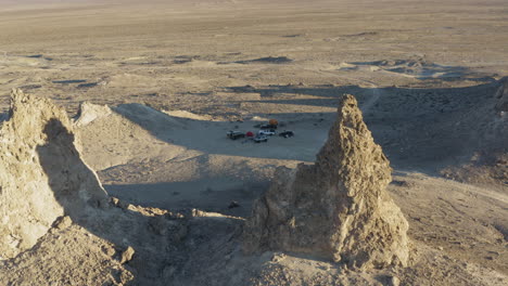 Aerial-shot-of-2-large-pinnacles-overlooking-a-camping-site-with-vehicles-in-the-california-Desert