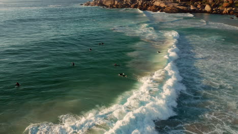 Surfers-Catch-And-Ride-The-Wave-On-Llandudno-Beach,-Cape-Town,-South-Africa---aerial-drone-shot