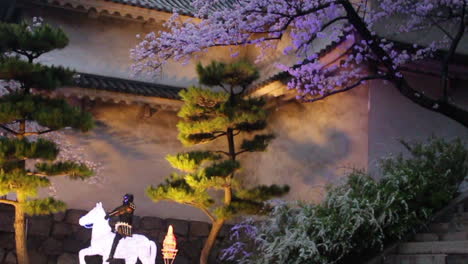 Kippvideo-Eines-Kirschblütenbaums,-Der-Nachts-Von-Künstlichem-Licht-Beleuchtet-Wird,-Und-Eines-Samurai,-Der-Auf-Einem-Pferd-Reitet