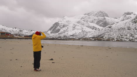 Man-Taking-Pictures-Of-Winter-Landscape-And-Snowy-Mountain-Range-Of-Lofoten-Norway---wide-shot