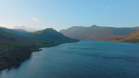 CRUMMOCK-WATER-Lake-District-Unesco-National-Park,-Aerial-Sunrise-push-forward-over-lake-with-sun-dappled-mountains