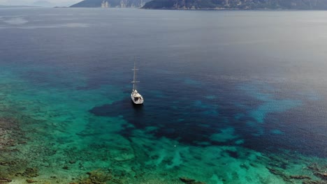 Aerial-View-Of-Sailboat-Anchored-In-The-Blue-Sea-With-Coral-Reefs-Under-The-Clear-Water