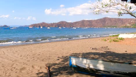 Wooden-boat-on-tropical-beach-with-green-leaves-trees-on-a-sunny-day,-Coco-Beach-in-Guanacaste,-Costa-Rica