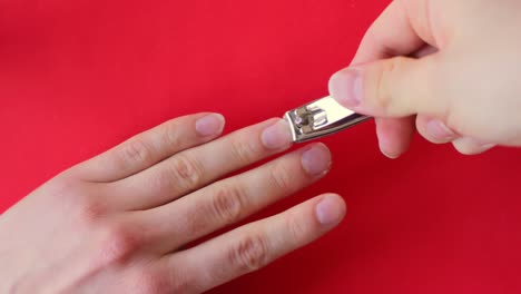 Looking-down-at-a-person-clipping-their-nails-with-a-metal-nail-clipper-on-a-red-background