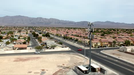 Cell-tower-on-the-foreground-in-a-Las-Vegas-suburb-with-mountains-beyond-the-valley---ascending-aerial-view