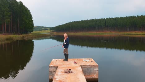 A-girl-fishing-from-a-pier-on-a-beautiful-calm-lake-in-a-forest