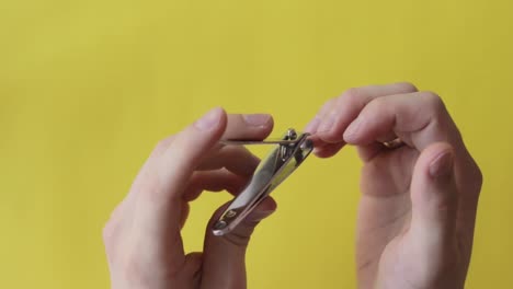 Nails-cutting,-top-down-view-of-white-hands-using-clipper,-yellow-background,-static-closeup