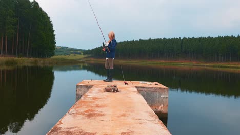 A-woman-fishing-for-bass-from-a-pier-in-a-beautiful-forest-lake