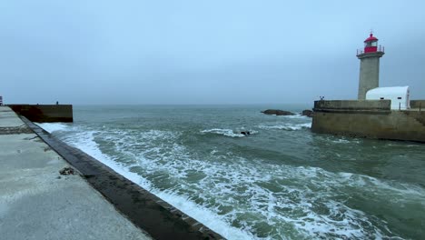 Zeitlupe-Stürmischer-Wellen,-Die-An-Einem-Bewölkten-Dunklen-Tag-Gegen-Die-Wand-Im-Hafen-Von-Porto-Mit-Leuchtturm-Schlagen