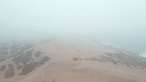 Aerial-dolly-out-of-orange-sand-dunes-in-a-hillside-near-the-sea-on-an-overcast-foggy-day-in-Concon,-Chile