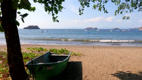 Wooden-boat-on-tropical-beach-with-a-tree-on-a-sunny-day,-Coco-Beach-in-Guanacaste,-Costa-Rica