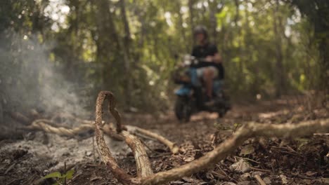 Two-Male-Riders-Driving-Along-The-Path-In-The-Forest-With-Smoky-Burning-Dry-Twigs-Left-By-Campers